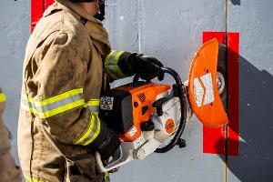 A firefighter cutting a metal wall with a saw