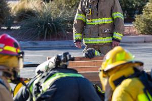 A supervising firefighter watching over three firefighters training