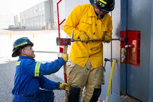 Two firefighters prying open a container on the wall with a crowbar