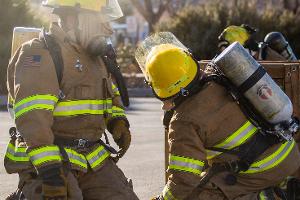 Two firefighters kneeling down, holding a firehose