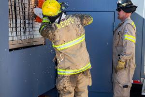 Two firefighters cutting a brick wall with a saw