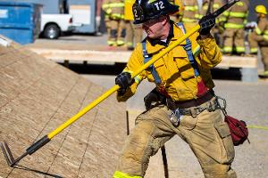 A firefighter opening plywood with a garden rake