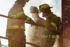 Three firefighters holding onto a rail in smoke