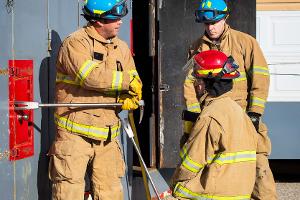 Three firefighters prying open a container on the wall with a crowbar
