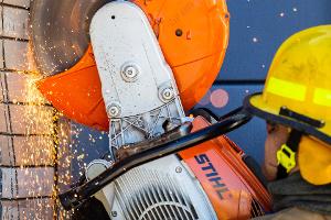 A firefighter cutting a brick wall with a saw