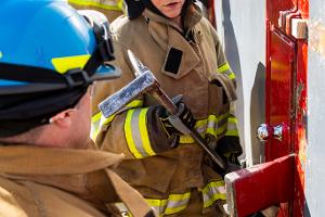 Two firefighters prying open a container on the wall with a crowbar