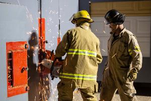Two firefighters cutting a metal wall with a saw