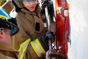 Two firefighters prying open a container on the wall with a crowbar