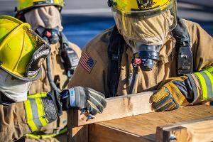 Two firefighters next to a small wooden tunnel