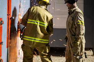 Two firefighters cutting a metal wall with a saw