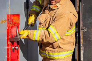 A firefighter prying open a container on the wall with a crowbar