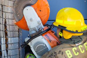 A firefighter cutting a brick wall with a saw