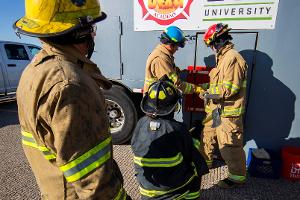 Four firefighters prying open a container on the wall with a crowbar