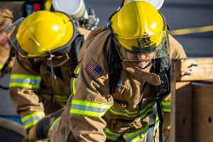 Firefighters crawling towards a small wooden tunnel