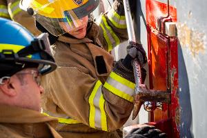 Two firefighters prying open a container on the wall with a crowbar