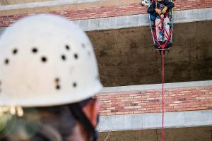 A person repelling from a building in a gurney type harness