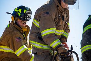 Two firefighters cutting plywood with a saw