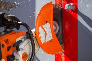 A firefighter cutting a metal wall with a saw