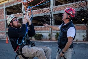 Man hanging on a rope with harness being instructed by another man