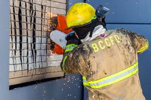 A firefighter cutting a brick wall with a saw