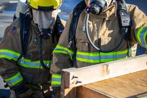 Two firefighters next to a small wooden tunnel