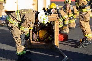 Firefighters line up to crawl through a small wooden tunnel