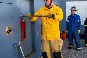 Two firefighters prying open a container on the wall with a crowbar