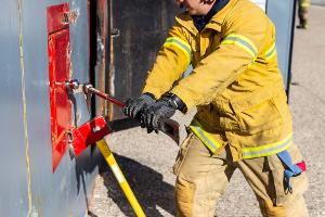 A firefighter prying open a container on the wall with a crowbar