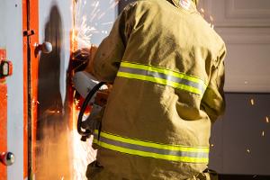 A firefighter cutting a metal wall with a saw