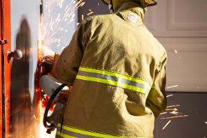 A firefighter cutting a metal wall with a saw