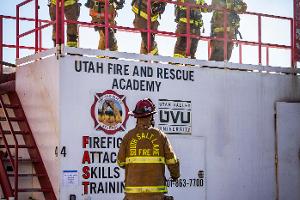 Five firefighters behind a rail in the air watching another firefighter on the ground