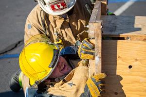 Two firefighters training, with one going through a small wooden tunnel