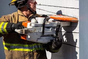 A firefighter cutting a brick wall with a saw