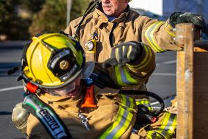 Two firefighters training, with one going through a small wooden tunnel