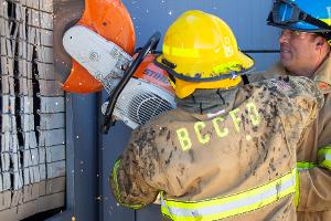 Two firefighters cutting a brick wall with a saw