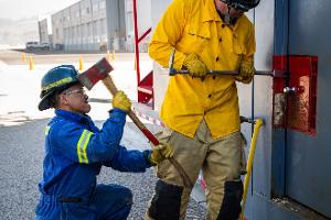 Two firefighters prying open a container on the wall with a crowbar