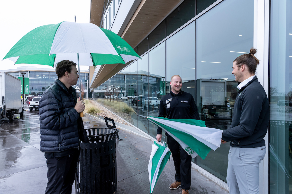 Event ambassadors help those in the rain with umbrellas at an event in the Keller building