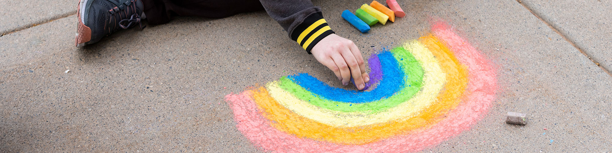 Close up of a hand making a chalk drawing of a rainbow on a sidewalk