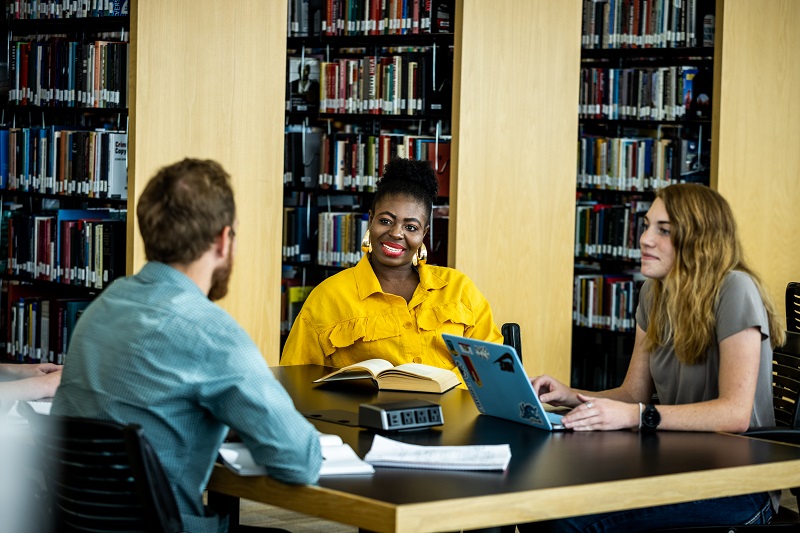 3 students talk at a table in the library.