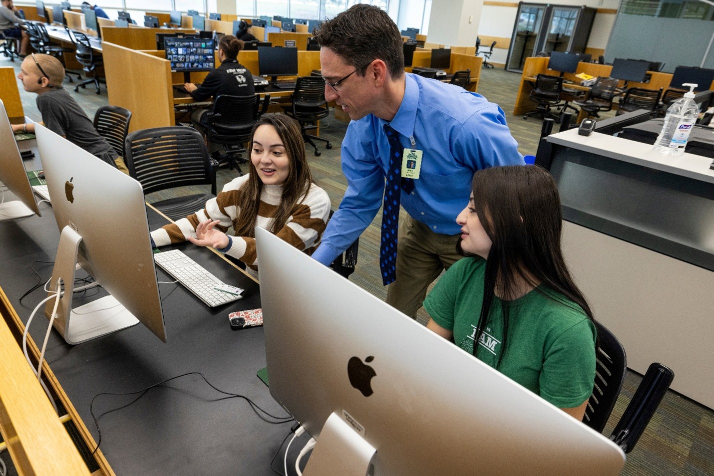 Students using computers in the library with the help of a librarian.