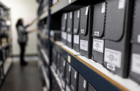 Stacks of archival collection with a worker in the background, blurred.