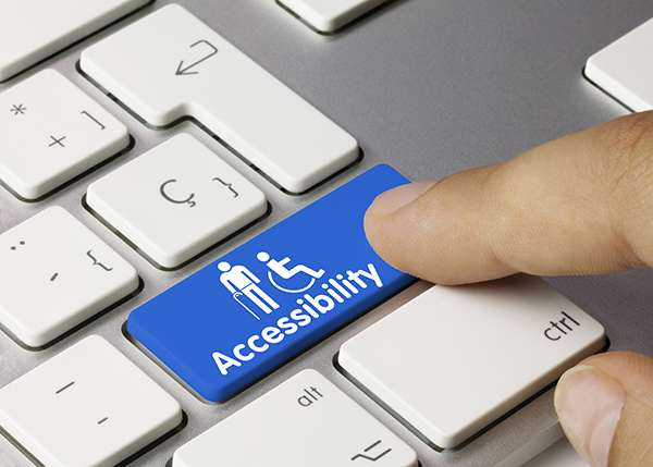 Image of a keyboard with a finger poised over a blue key. The key says accessibility and has pictures of a person with a cane and the wheelchair icon.