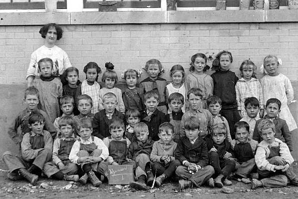 Black and white image of a group of about 35 children with a teacher or caretaker.