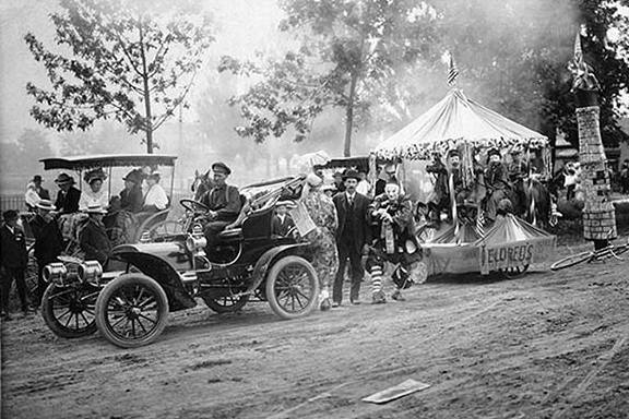 Black and white image of a gathering with old automobiles and a float