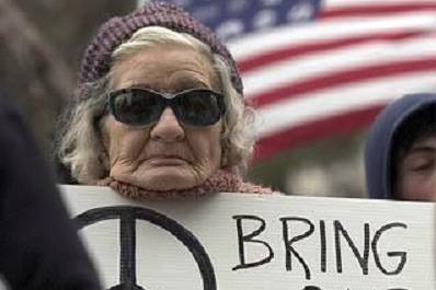 Woman with sunglasses and a beanie on, with a hand drawn protest sign.