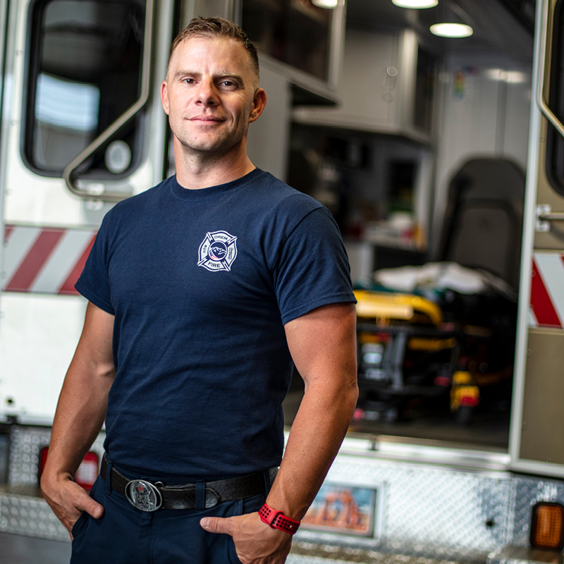 Male emergency worker stands in front of truck.