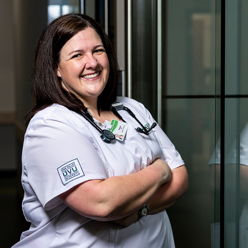 Female nurse smiles and crosses arms in scrubs.