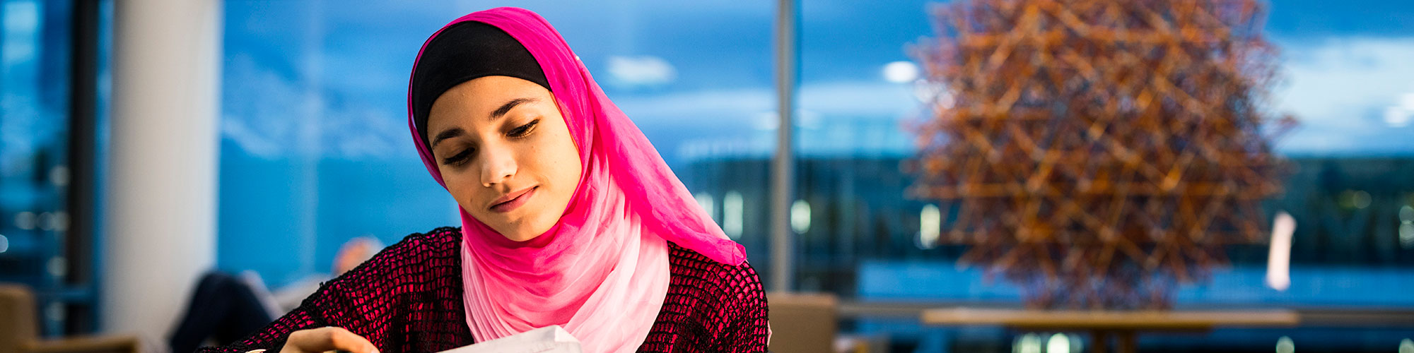 A woman with a head scarf reading something, smiling