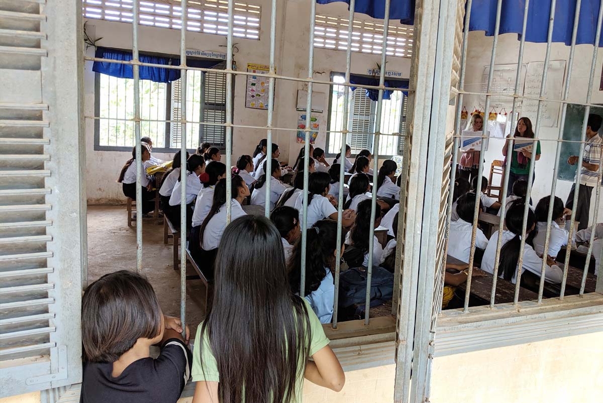 Two girls lean on the barred windows of the primary Cambodian school to lisen in on Professor Barthel's lecture.