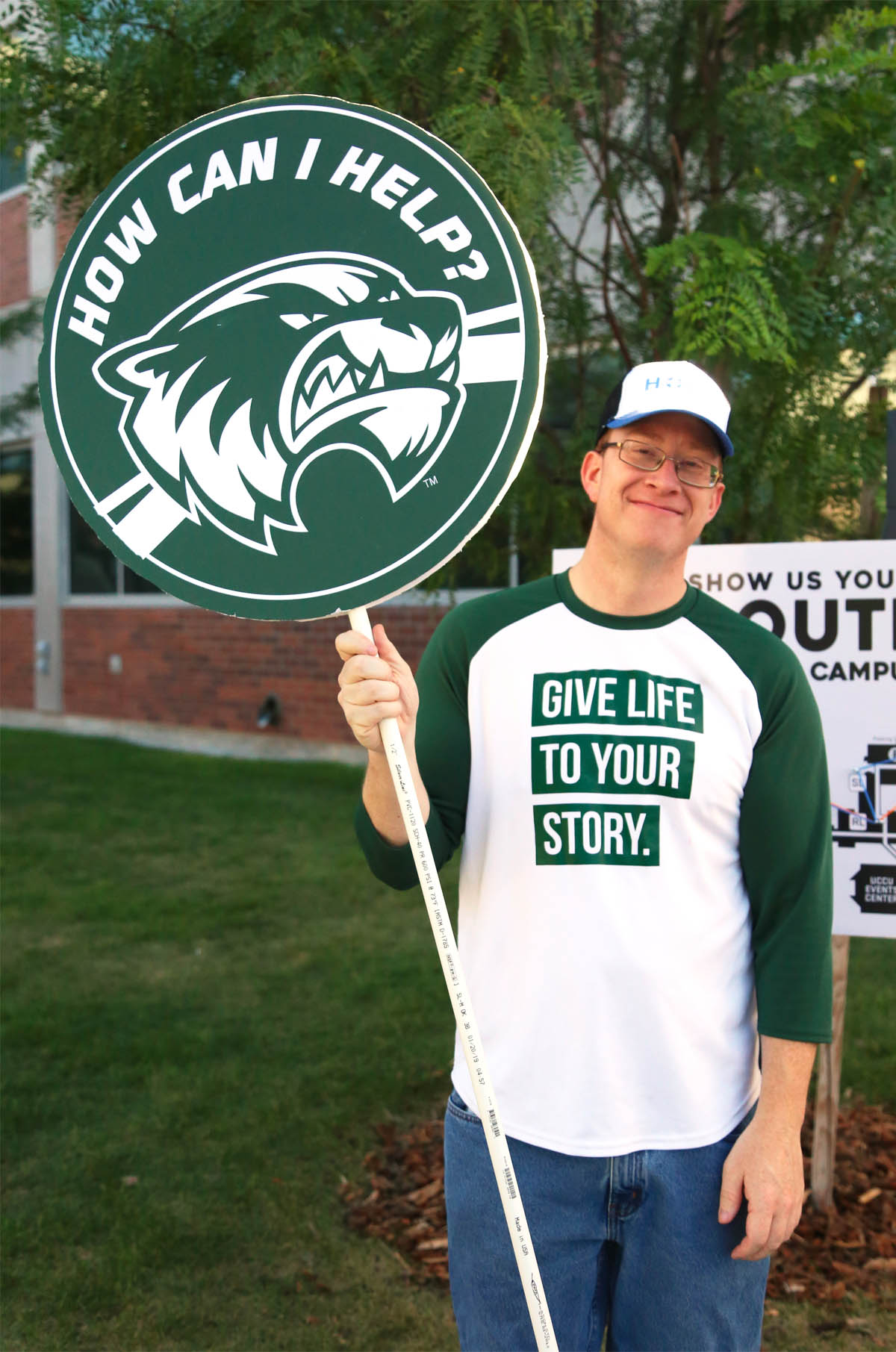 Student in UVU apparel holding a “how can I help?” sign. 